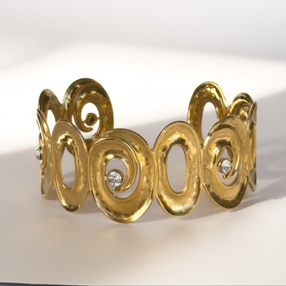 Gold bracelet with intricate design and embedded diamonds on a white background