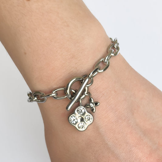 Silver chain bracelet with a clover-shaped charm on a wrist against a white background